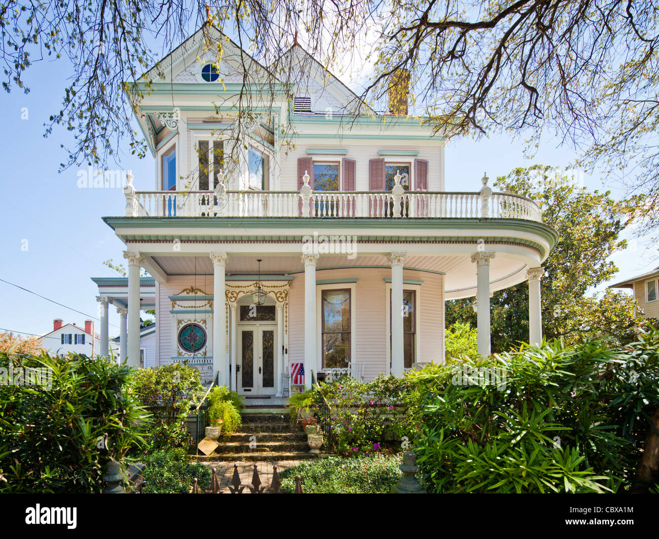 A Victorian-style mansion in New Orleans' Garden District with an iron-lace porch, lush greenery, and morning sunlight filtering through oak trees, real travel photography style