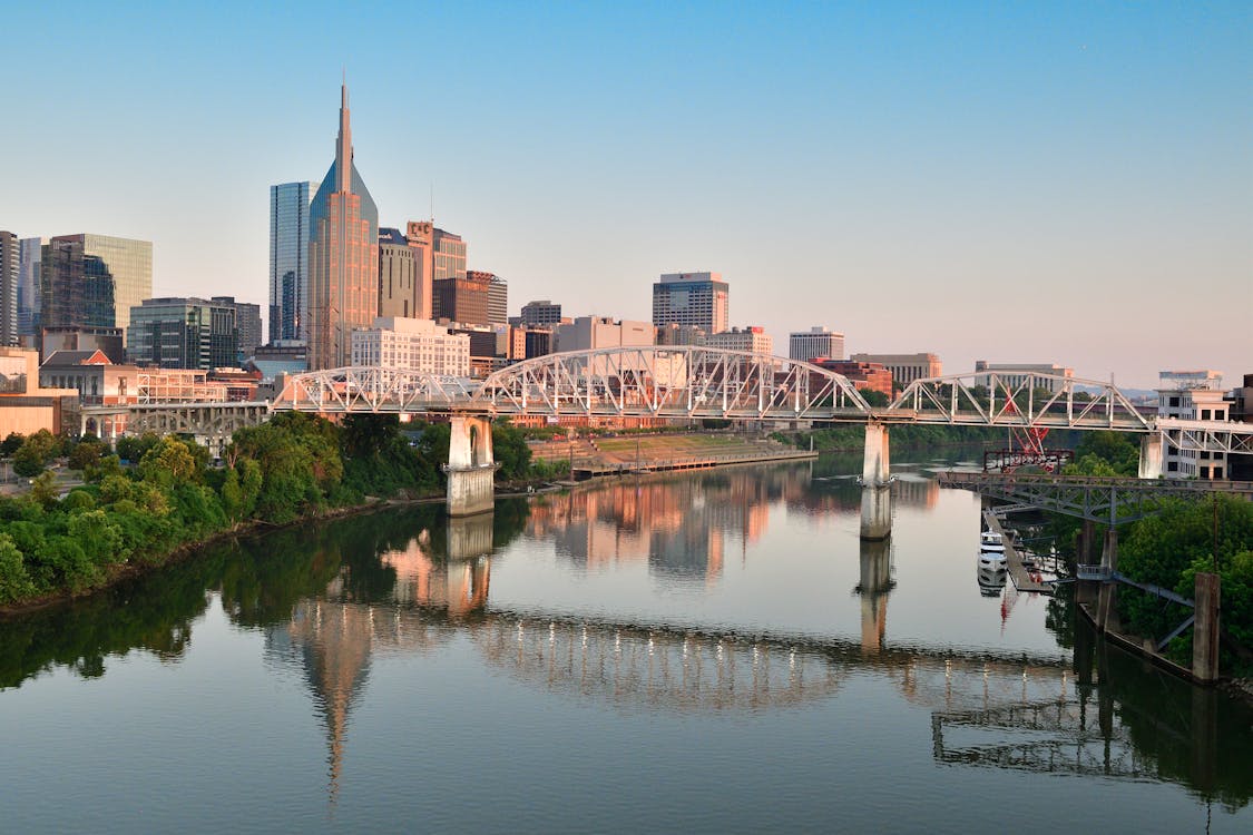A bright morning view of the Nashville skyline from the Cumberland River waterfront with pedestrians on a riverside path