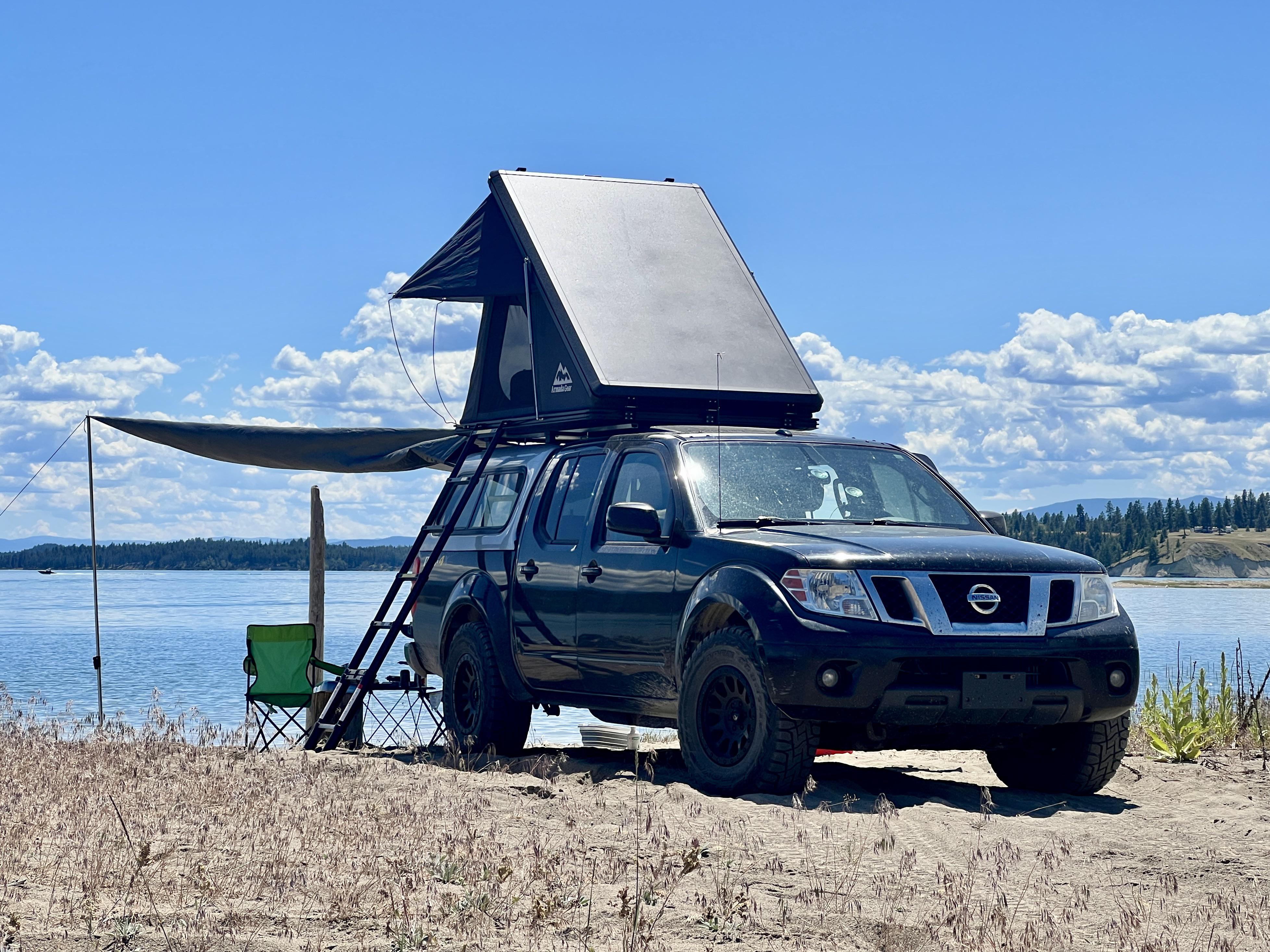 A camper washing a small pot at a backcountry campsite with a compact stove and a sealed trash bag nearby, evening light in a pine forest, realistic photography