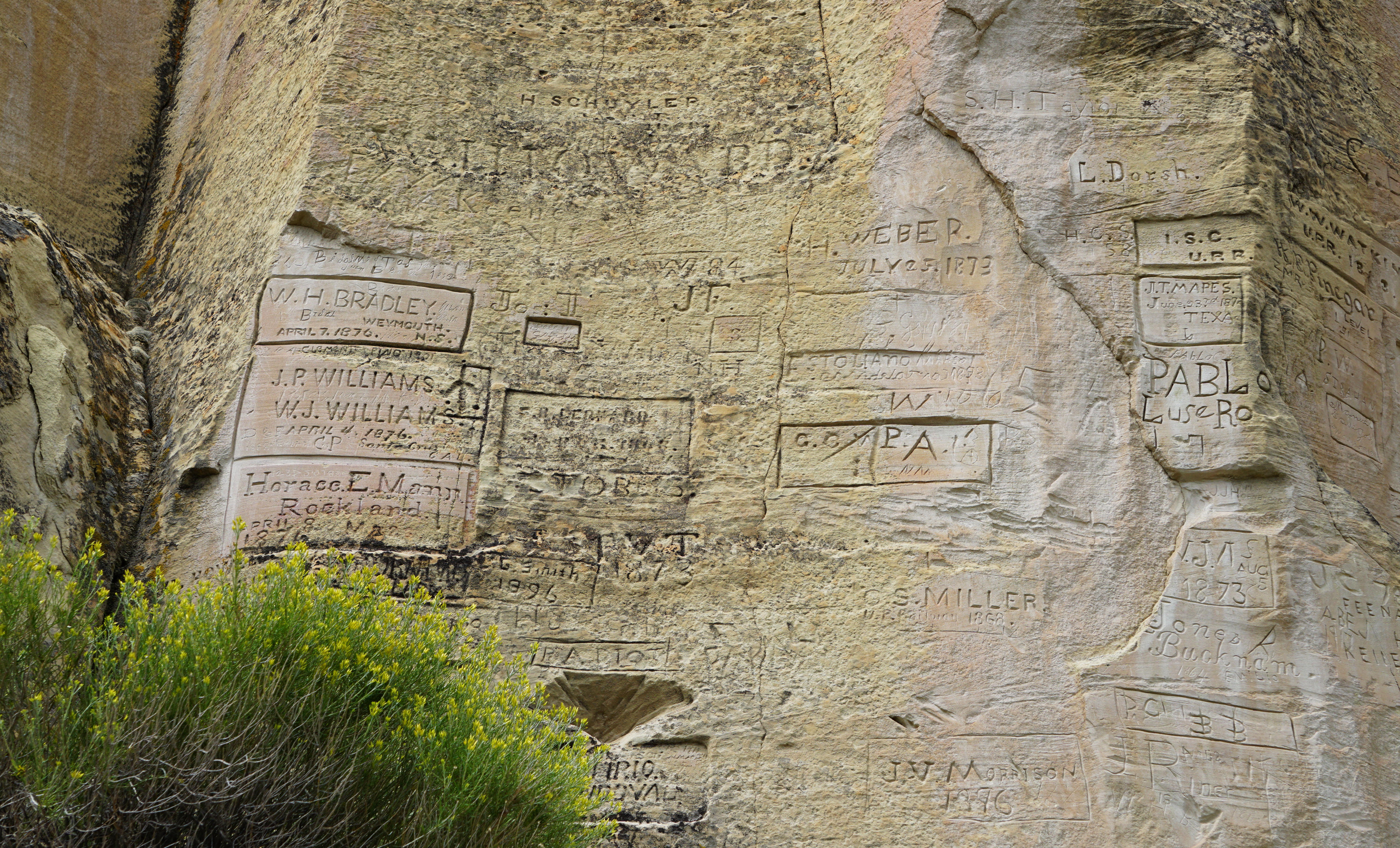 A close-up real photograph of weathered sandstone at El Morro National Monument with visible historic inscriptions etched into the rock surface, photographed at an angle that shows texture and depth