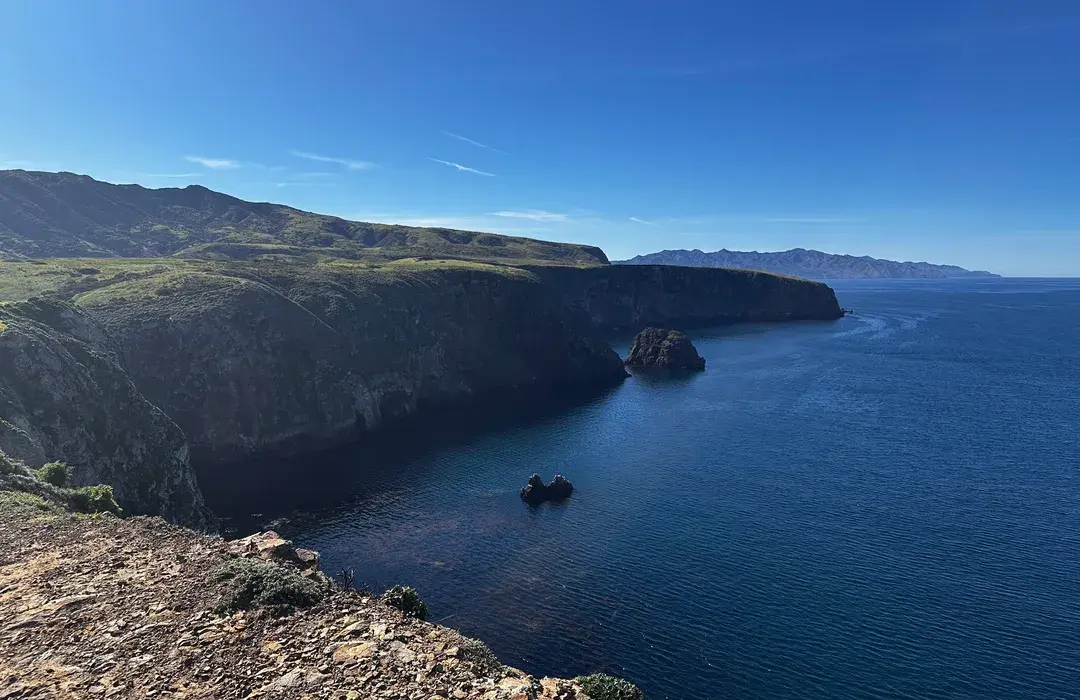 A coastal bluff viewpoint at Cavern Point on Santa Cruz Island with turquoise ocean water, rugged cliffs, and a narrow trail leading to the overlook