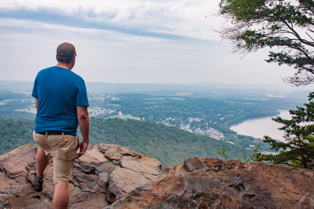A day hiker sitting on a rocky overlook, unpacking a simple trail lunch from a backpack with mountains in the background, natural light photography style