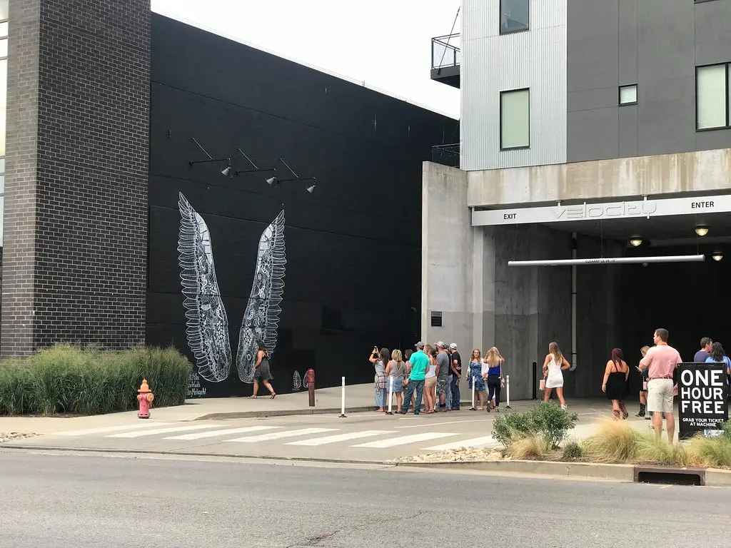 A daytime street scene in Nashville's Gulch neighborhood with a large colorful wall mural and pedestrians walking past modern storefronts