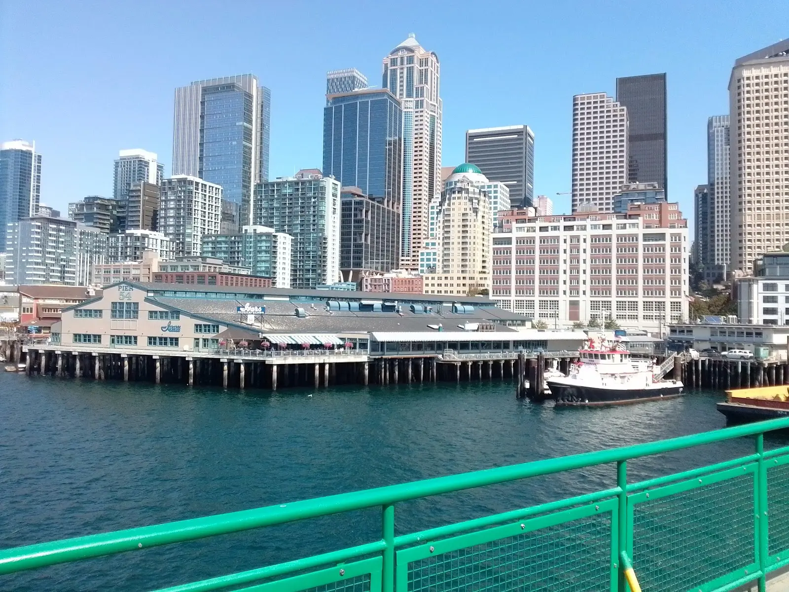 A daytime view of Seattle's waterfront piers with a ferry moving across Elliott Bay and the city rising behind it, natural light travel photo