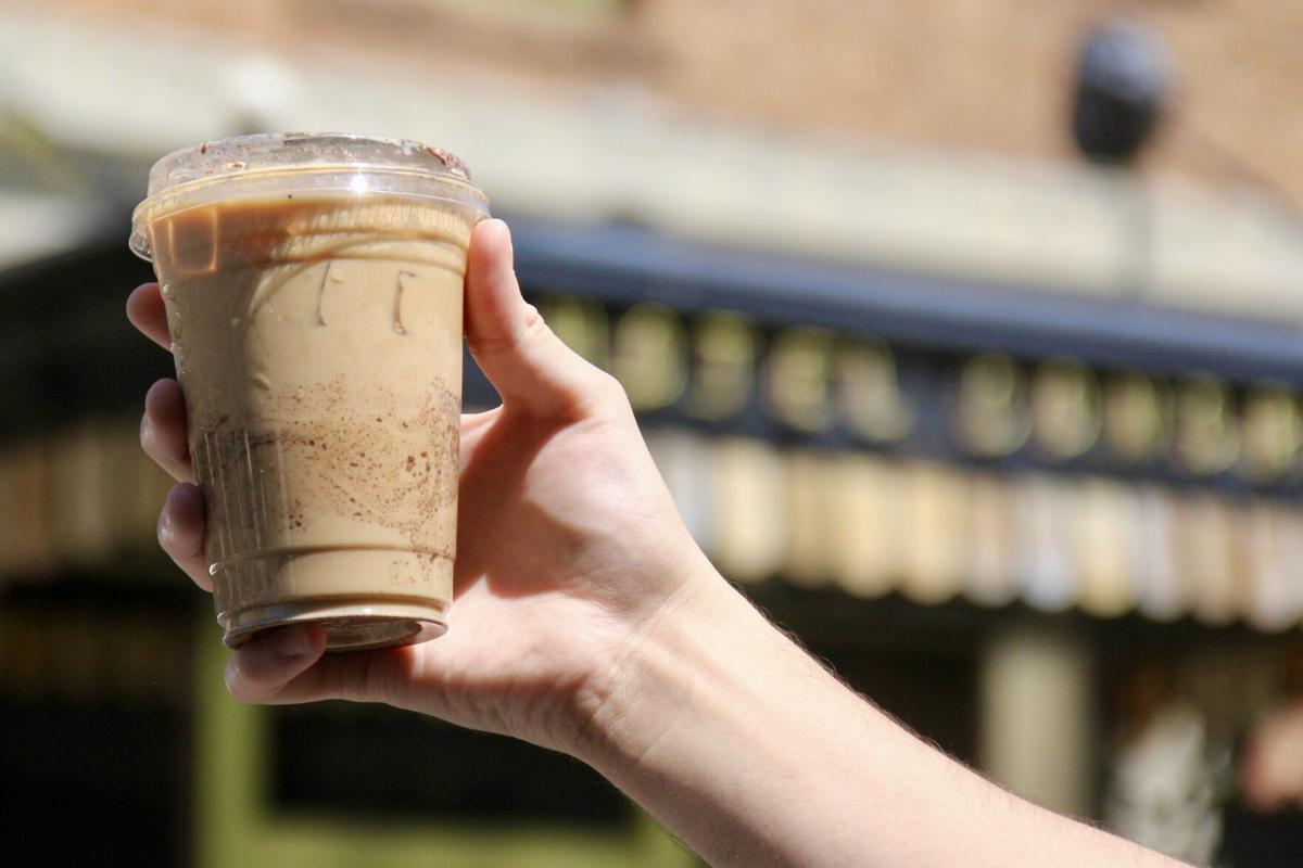 A dusty hiking backpack resting beside a small outdoor cafe table in a desert town, with a glass of iced coffee and sunlit storefronts in the background