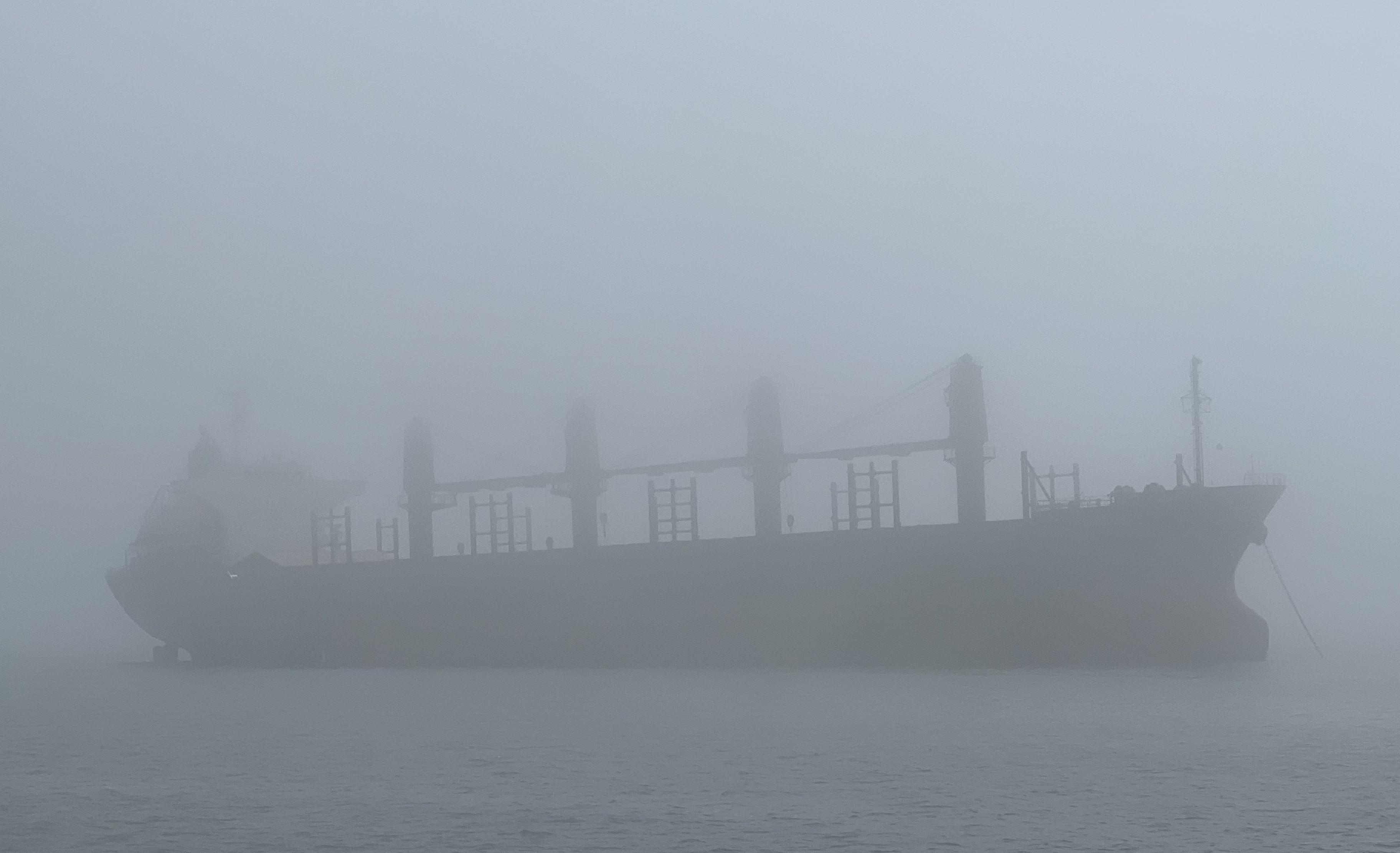 A ferry at Ventura Harbor partially shrouded in coastal fog with muted gray light and calm water, realistic travel photography