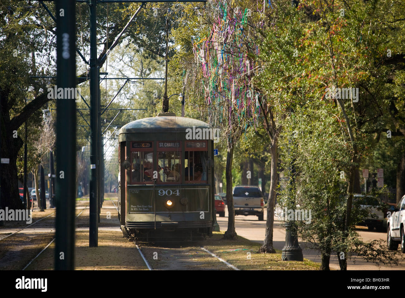 A green St. Charles streetcar rolling past large live oak trees and historic mansions in New Orleans on a bright afternoon, real travel photography style