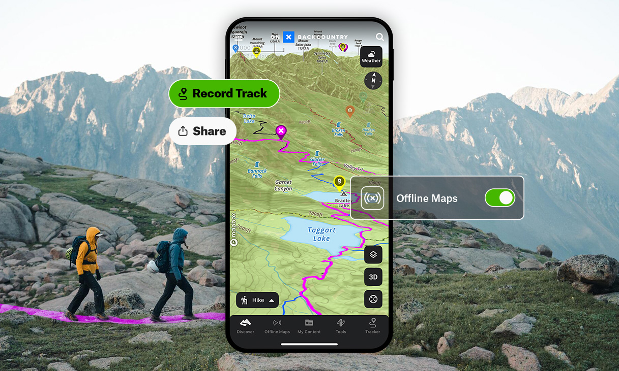 A hiker holding a smartphone showing an offline topographic map while standing on a rocky mountain trail with pine trees and distant peaks in soft morning light, realistic travel photography