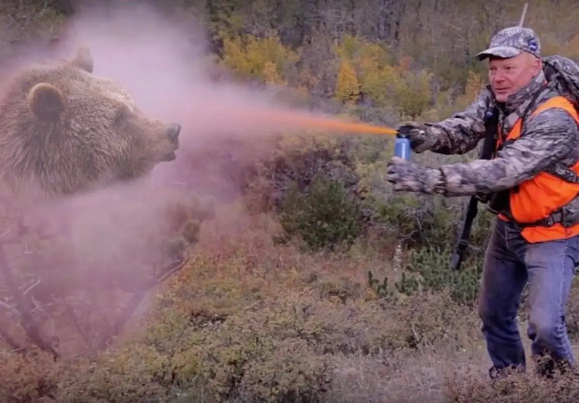 A hiker in outdoor clothing practicing a bear spray deployment in an open grassy field on a calm day, holding the canister out in front with arms slightly bent, realistic photography