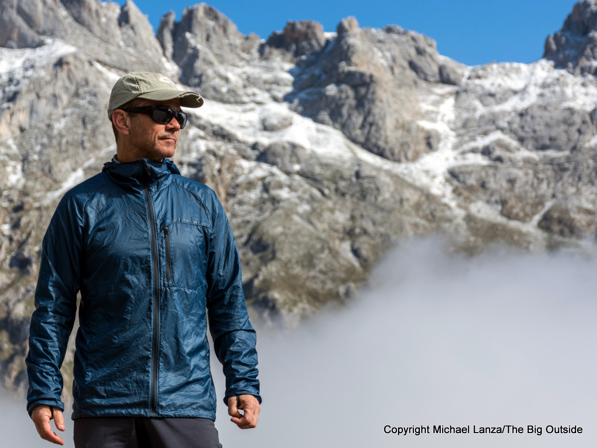 A hiker on an alpine ridge pulling on a lightweight wind shell over a base layer while clouds move in behind them, realistic outdoor photography