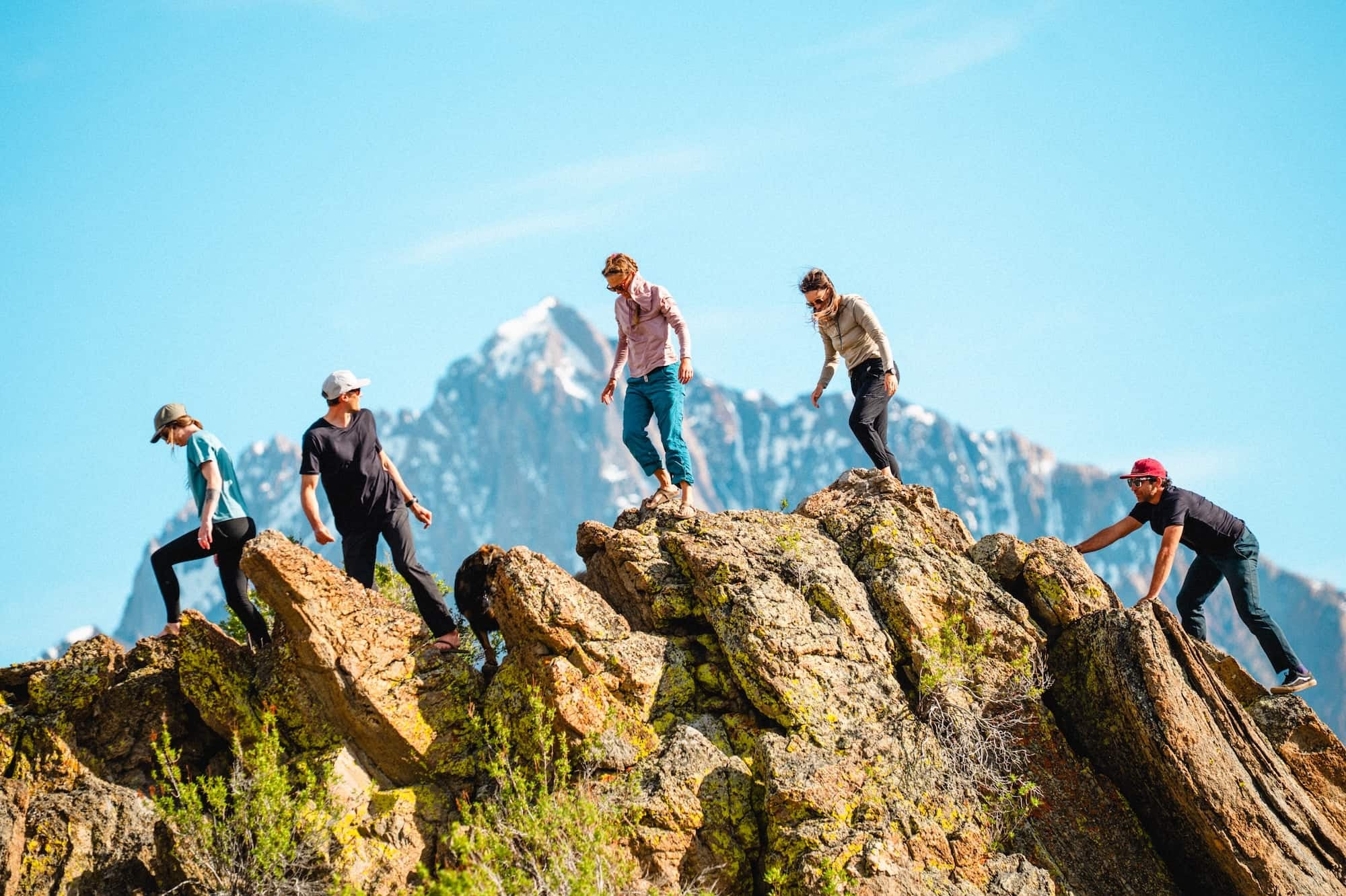 A hiker on an exposed sunny ridge wearing a hooded UPF sun shirt, sunglasses, and a neck gaiter pulled around the neck, with a small daypack, real outdoor photography