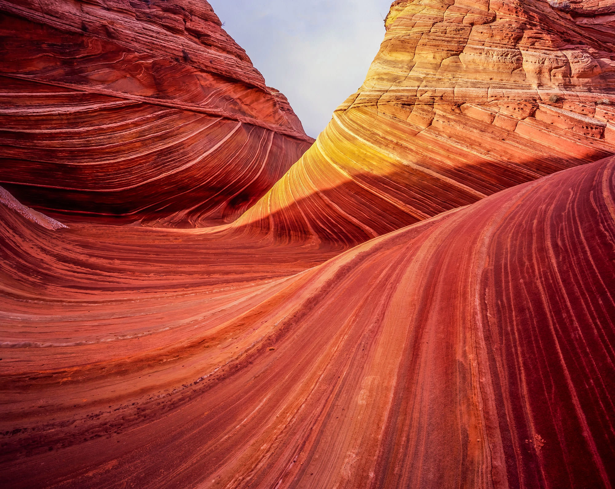 A hiker pausing on pale slickrock in Coyote Buttes North while checking a handheld GPS, with low desert hills and scattered cairns in the background