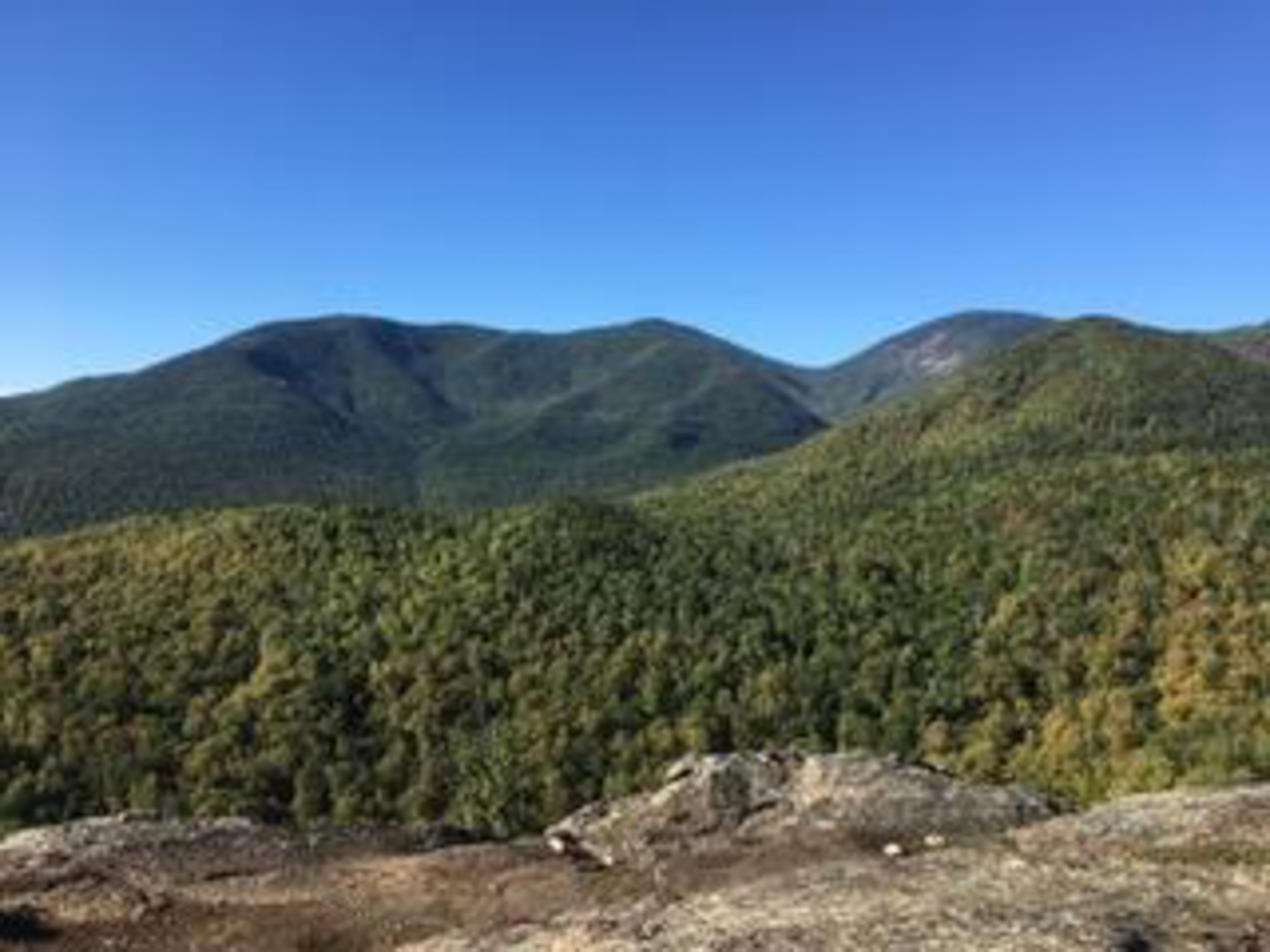 A hiker sitting on a rocky trail in early fall light, wrapping an elastic bandage around an ankle, with a small daypack open beside them, candid outdoor photograph