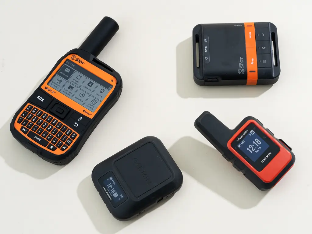 A hiker standing on a windy mountain ridge at golden hour holding a small satellite messenger device in one hand, realistic outdoor photograph