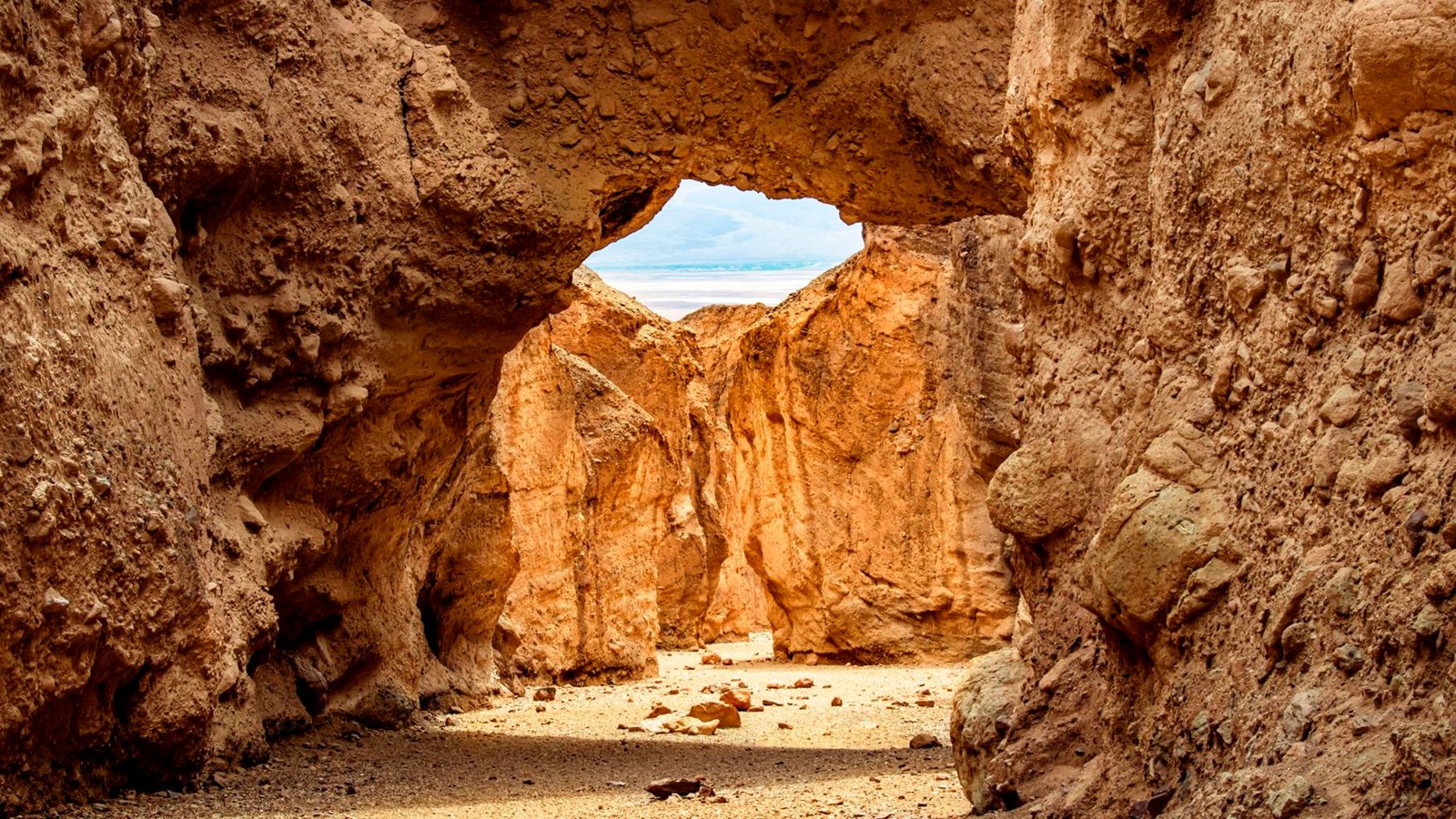 A large natural rock arch spanning a narrow canyon in Death Valley with hikers standing beneath it for scale, realistic outdoor photography
