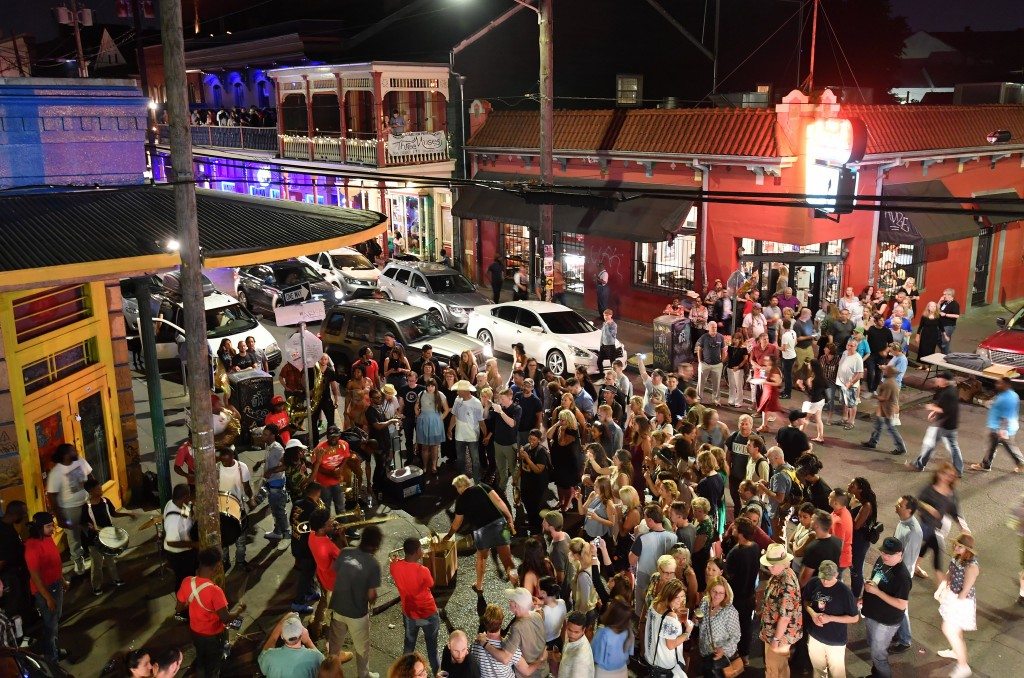 A lively nighttime scene on Frenchmen Street in New Orleans with people gathered outside a small music venue and warm neon light spilling onto the sidewalk, real travel photography style