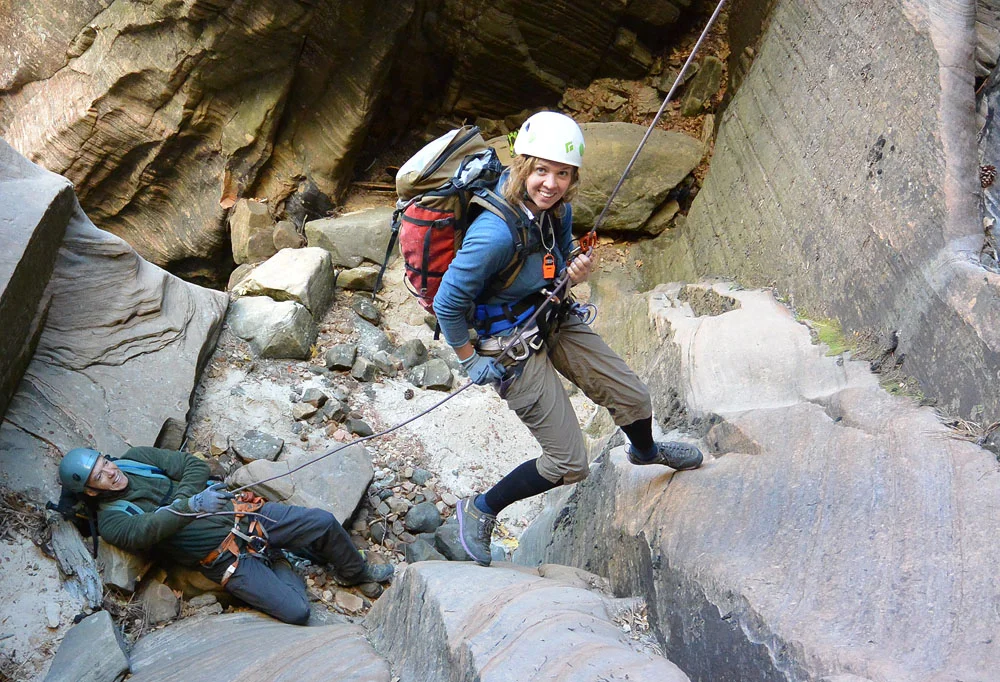 A neatly arranged set of canyoneering gear including helmet, harness, rope bag, dry bag, and neoprene socks on a sandstone slab in Zion National Park, outdoor gear photo