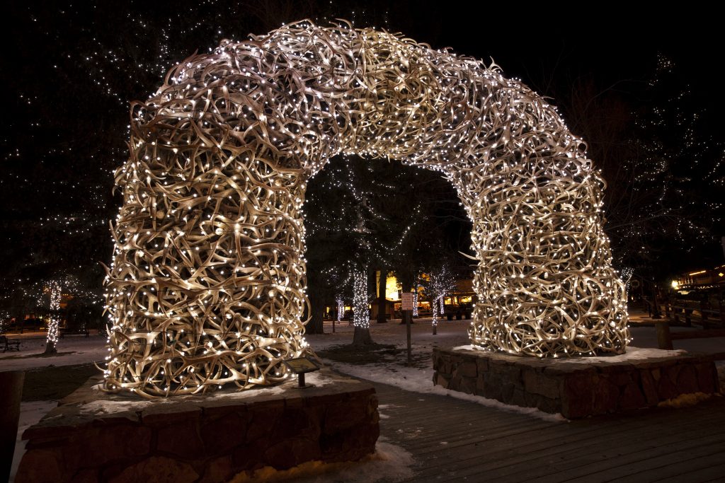 A photo of the Jackson, Wyoming town square at dusk with the elk antler arches and warm streetlights, people walking in the background, travel photo style