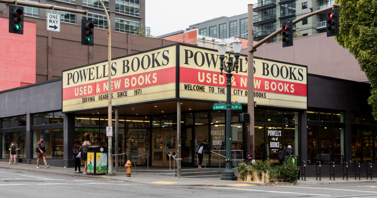 A photorealistic exterior street scene of Powell’s City of Books in Portland with pedestrians crossing at the corner on an overcast day, travel photography style