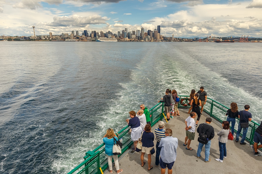 A photorealistic scene of a Washington State ferry crossing Puget Sound with the Seattle skyline in the background and passengers on the outdoor deck, late afternoon light, travel photography style