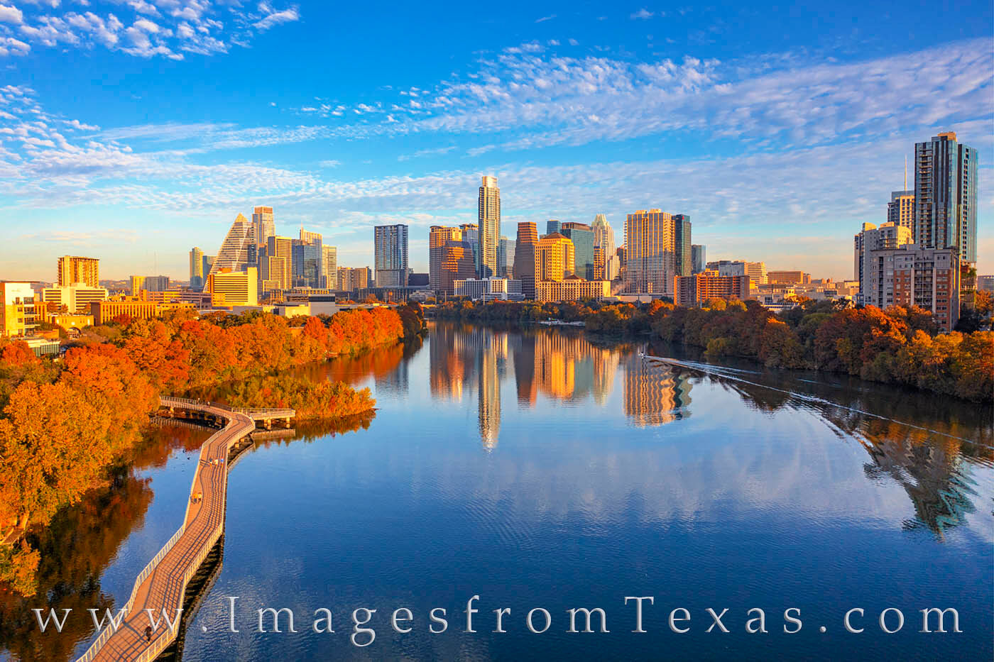 A real morning photo from the Lady Bird Lake trail with the Austin skyline reflecting in the water and runners passing on the path
