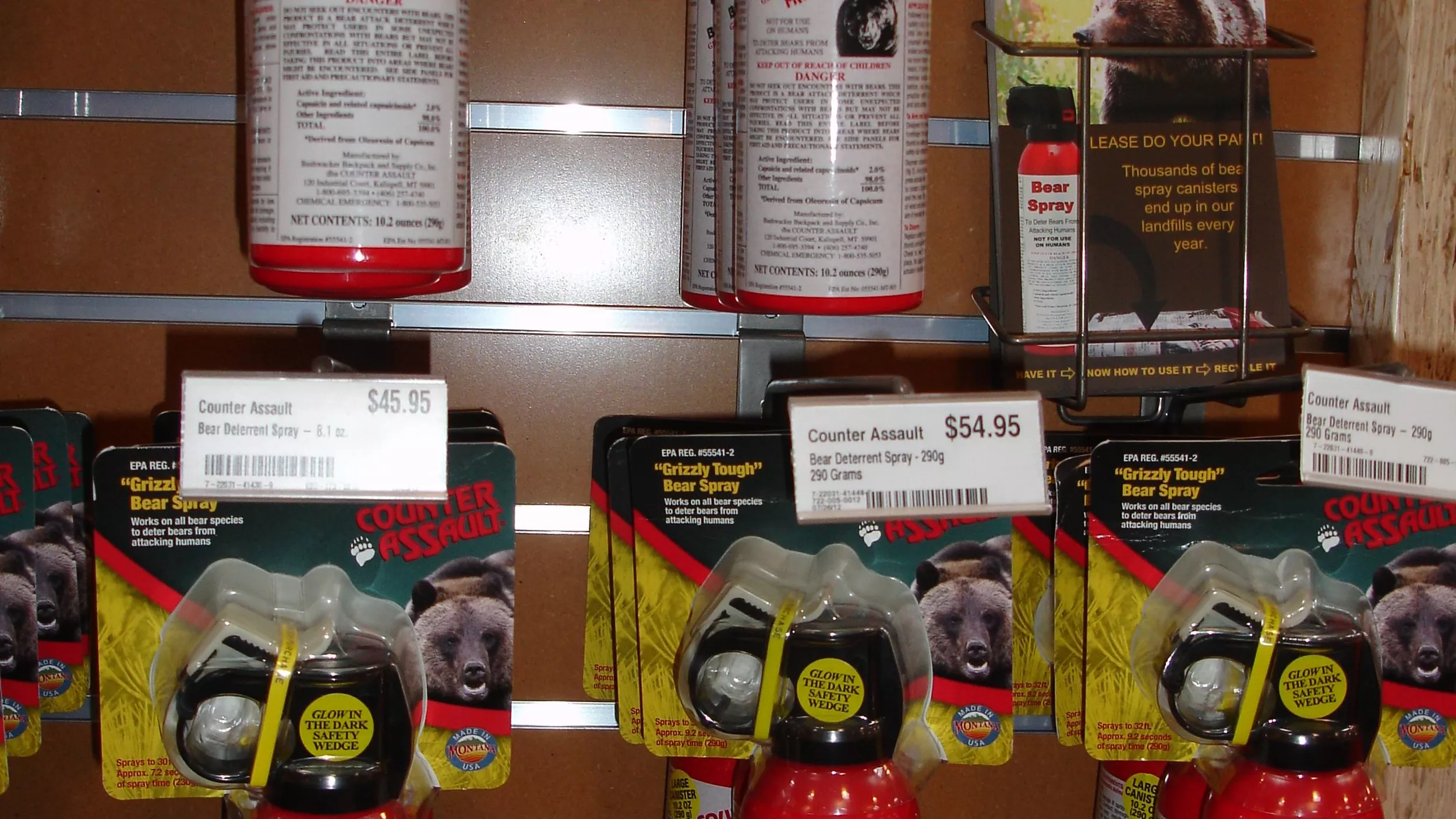 A real outdoor retail store shelf near an airport stocked with bear spray canisters and hiking safety items, shallow depth of field photography