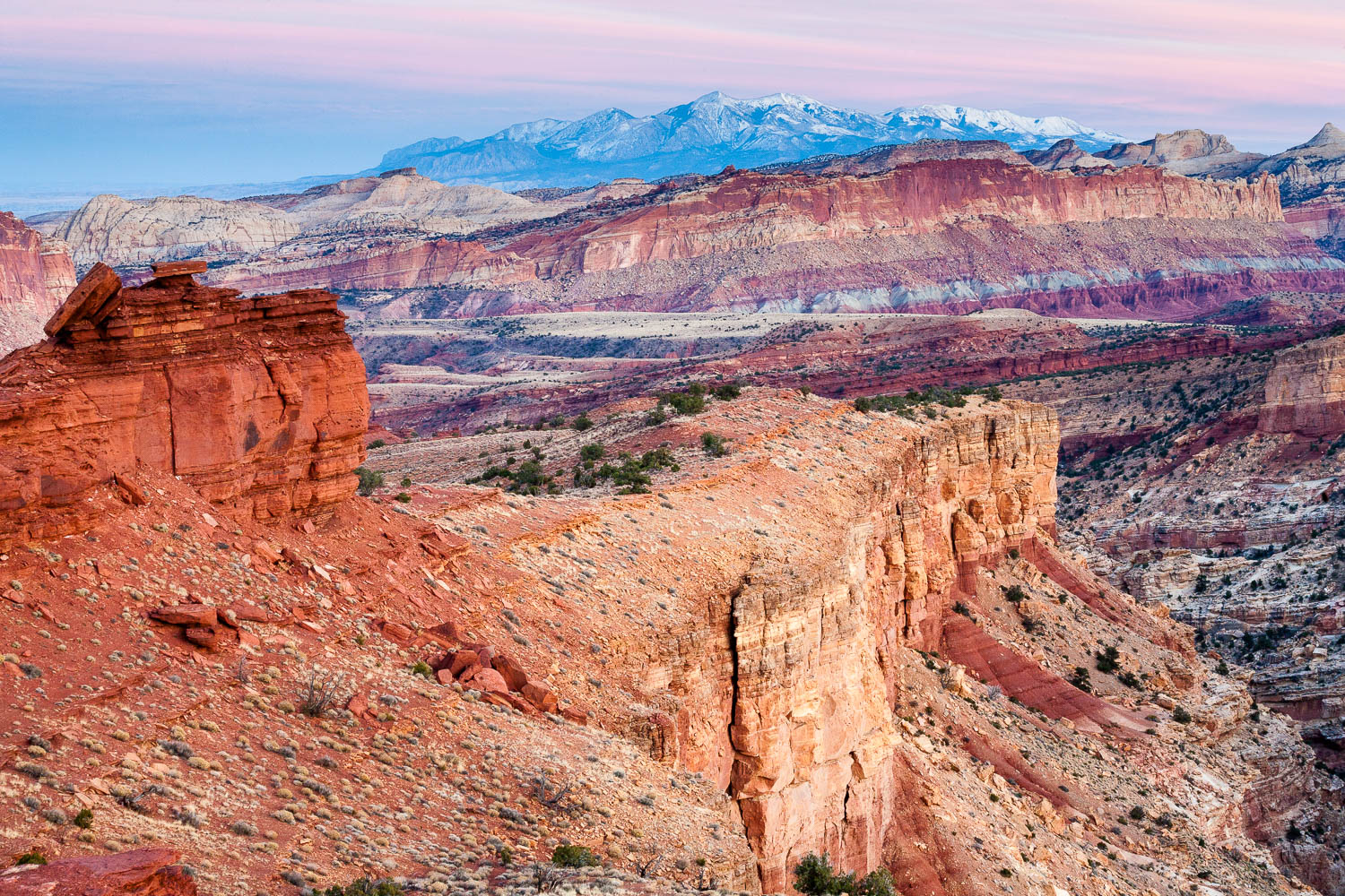 A real photo from Goosenecks Overlook in Capitol Reef at sunset, looking down at winding canyon bends with layered cliffs glowing orange