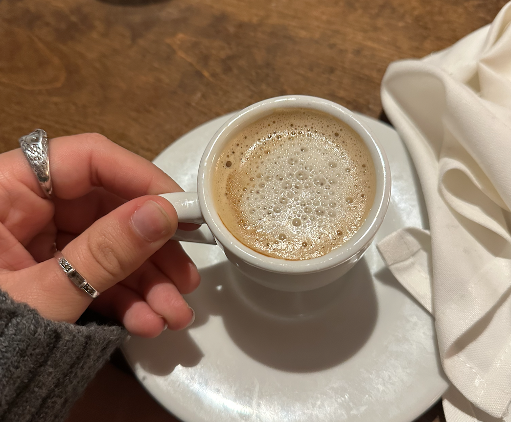 A real photo of a Miami barista pouring steamed milk into a small cortadito in a cozy cafe with warm lighting
