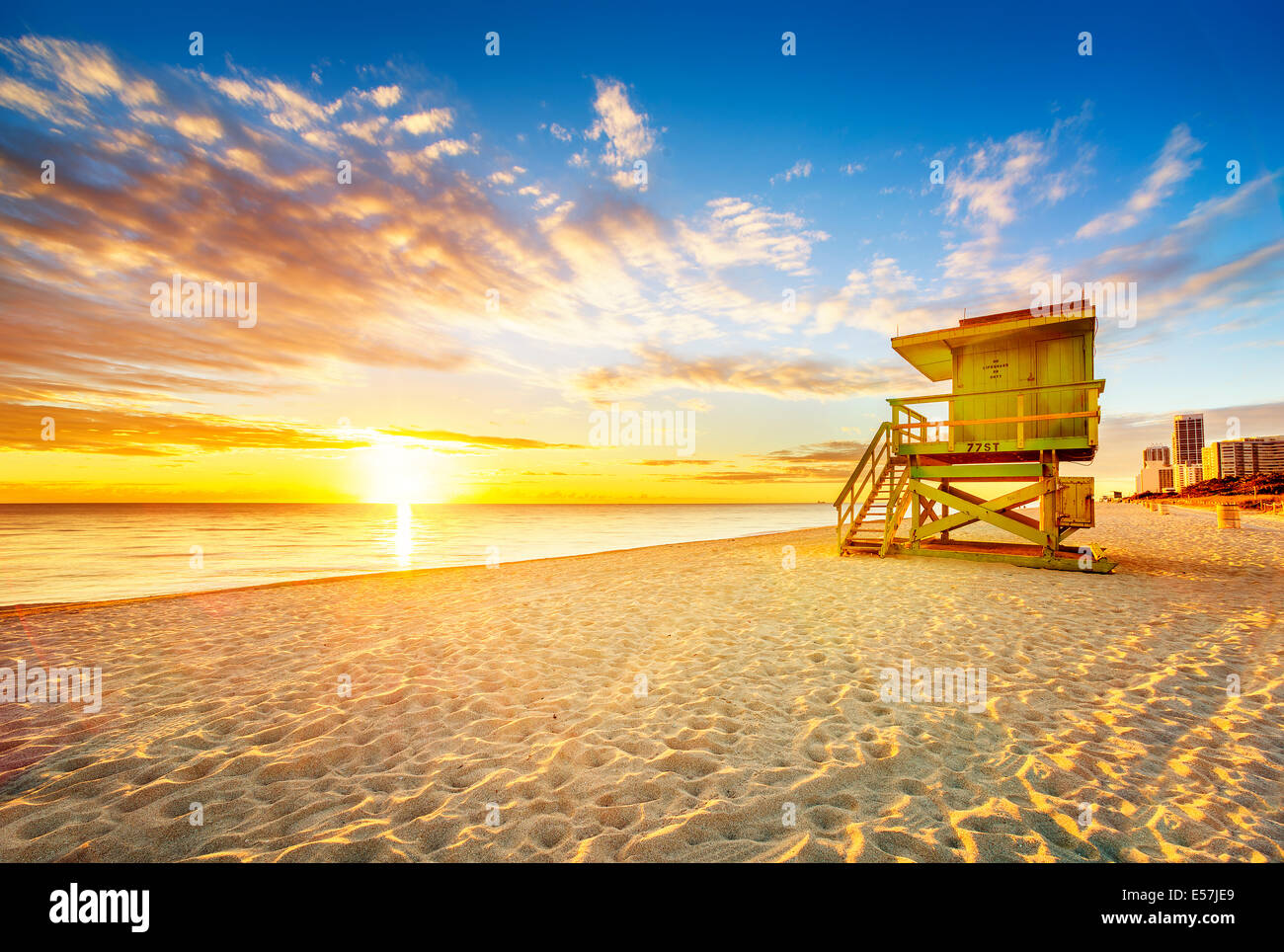 A real photo of a colorful lifeguard tower on Miami Beach at sunrise with a pastel sky and a few early walkers
