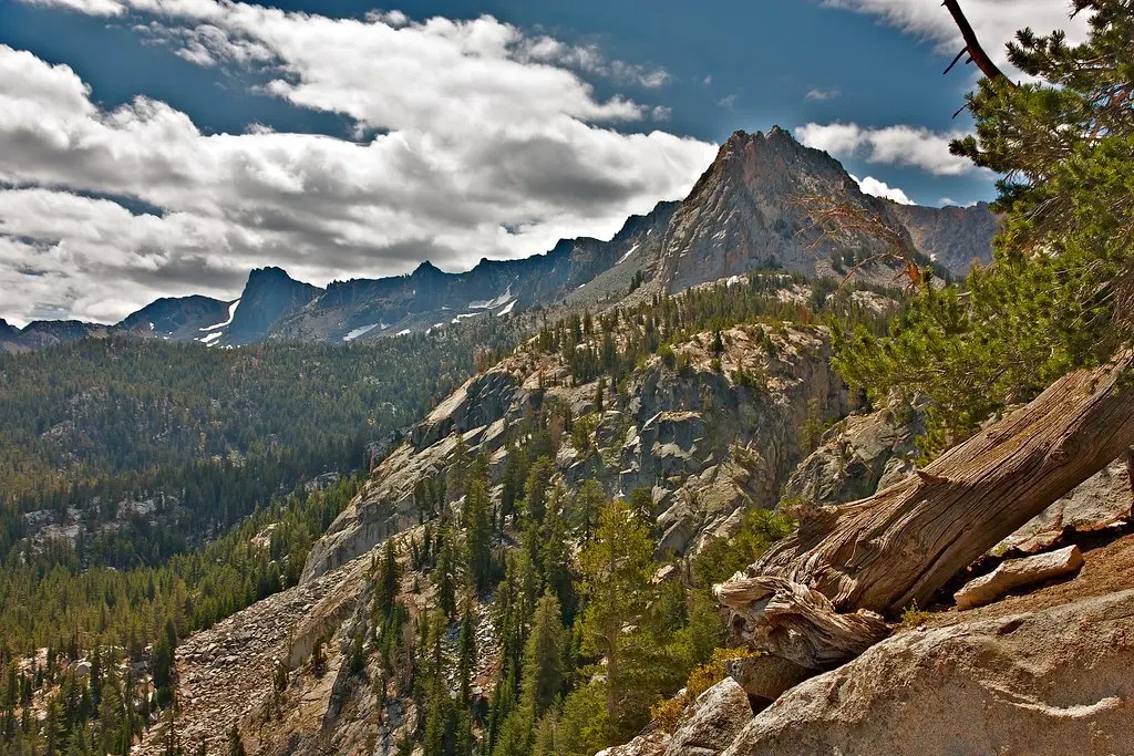 A real photo of a hiker on the Mammoth Crest trail walking along a granite ridge with expansive views of blue lakes and distant mountains in summer