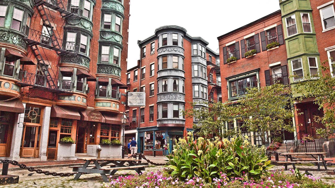 A real photo of a narrow North End Boston street with string lights, sidewalk diners, and brick buildings at dusk