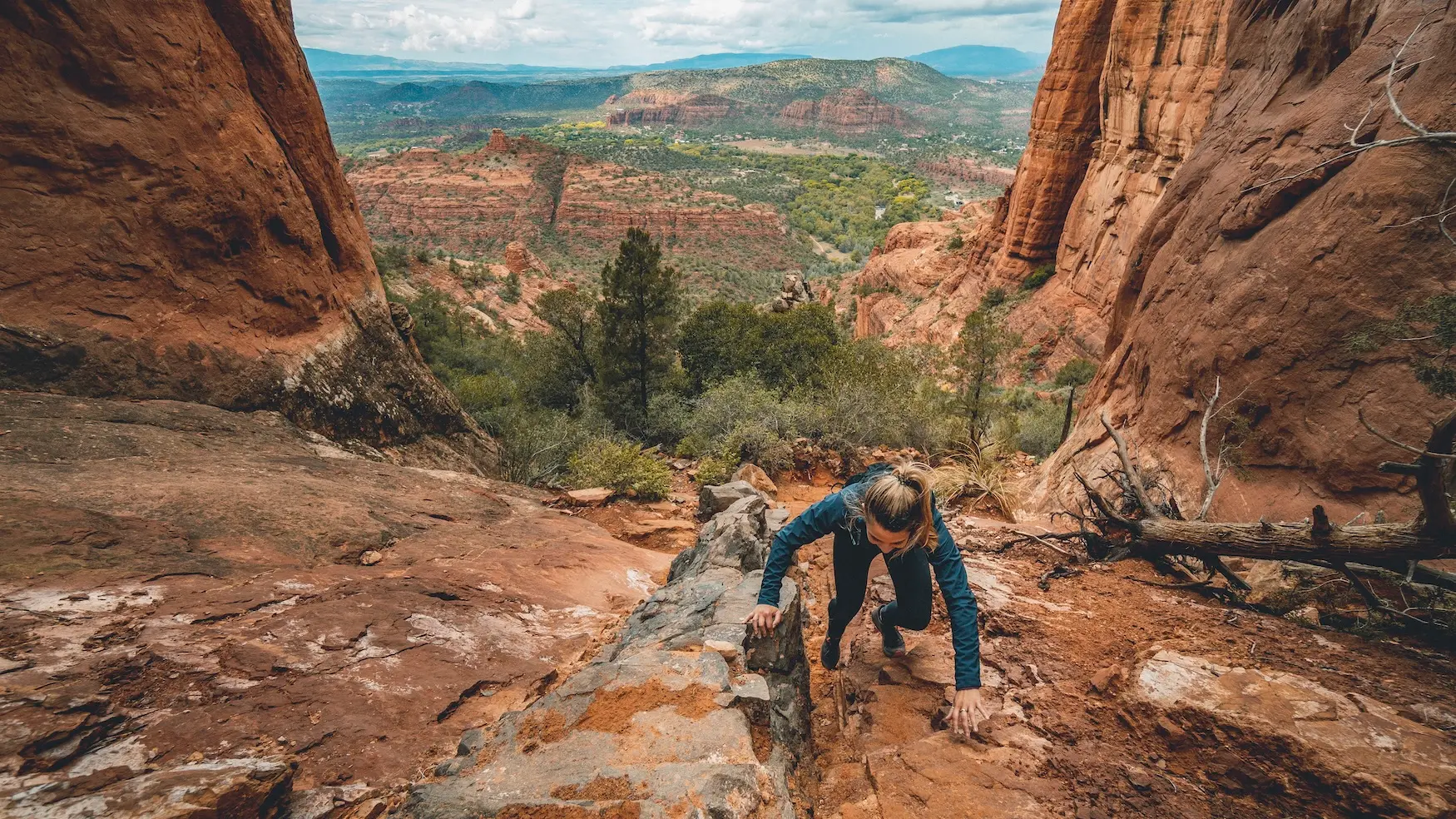 A real photo of hikers carefully scrambling up a steep slickrock section on Cathedral Rock Trail in Sedona, Arizona, using hands for balance on the sandstone