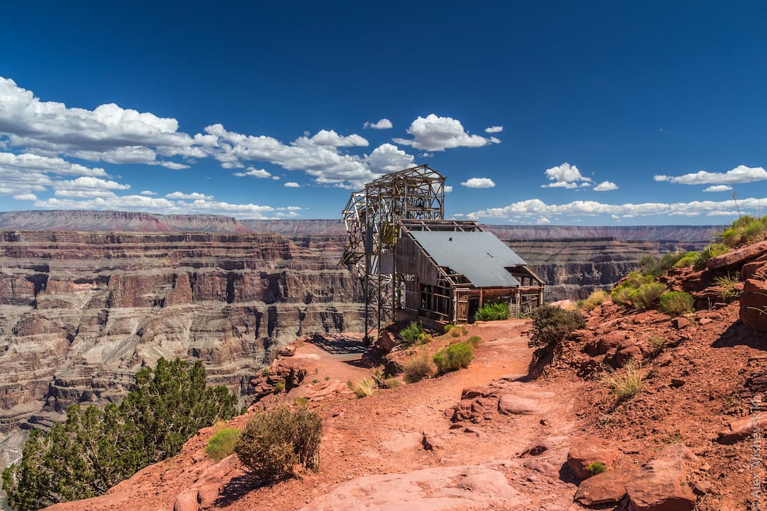 A real photograph at Guano Point on the Grand Canyon West side, visitors walking along a rocky viewpoint trail with sweeping canyon views under a clear blue sky