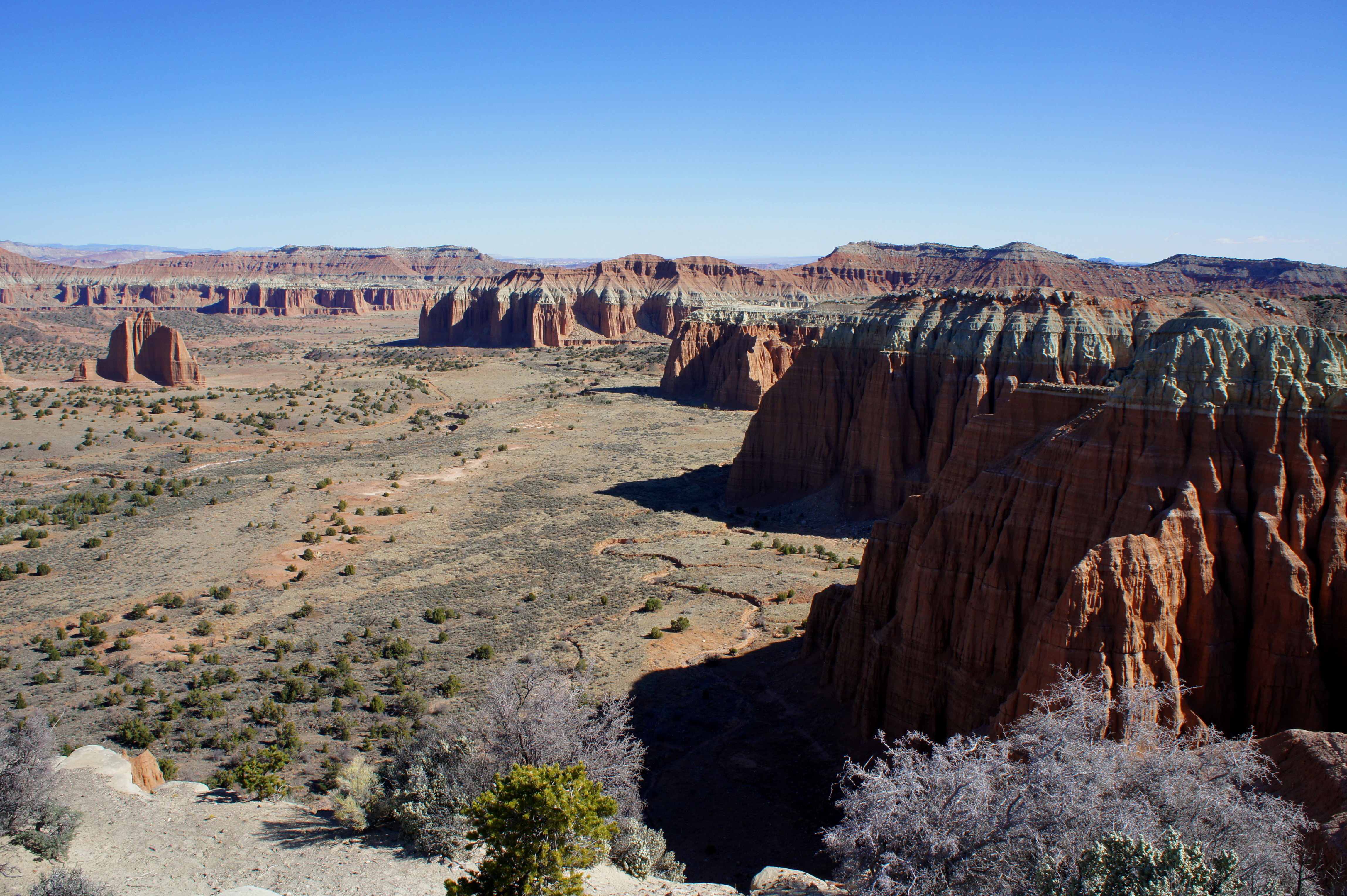 A real photograph from Cathedral Valley Overlook in Capitol Reef showing layered desert badlands and distant cliffs under a wide blue sky
