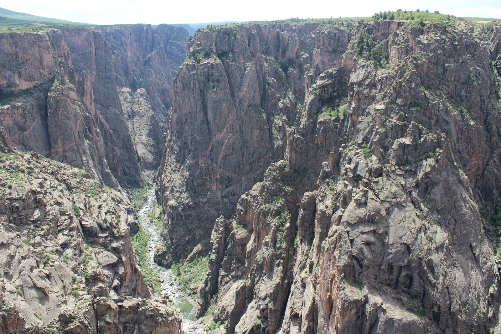 A real photograph from Chasm View on the North Rim with jagged dark canyon walls filling the frame and the Gunnison River visible as a thin ribbon far below