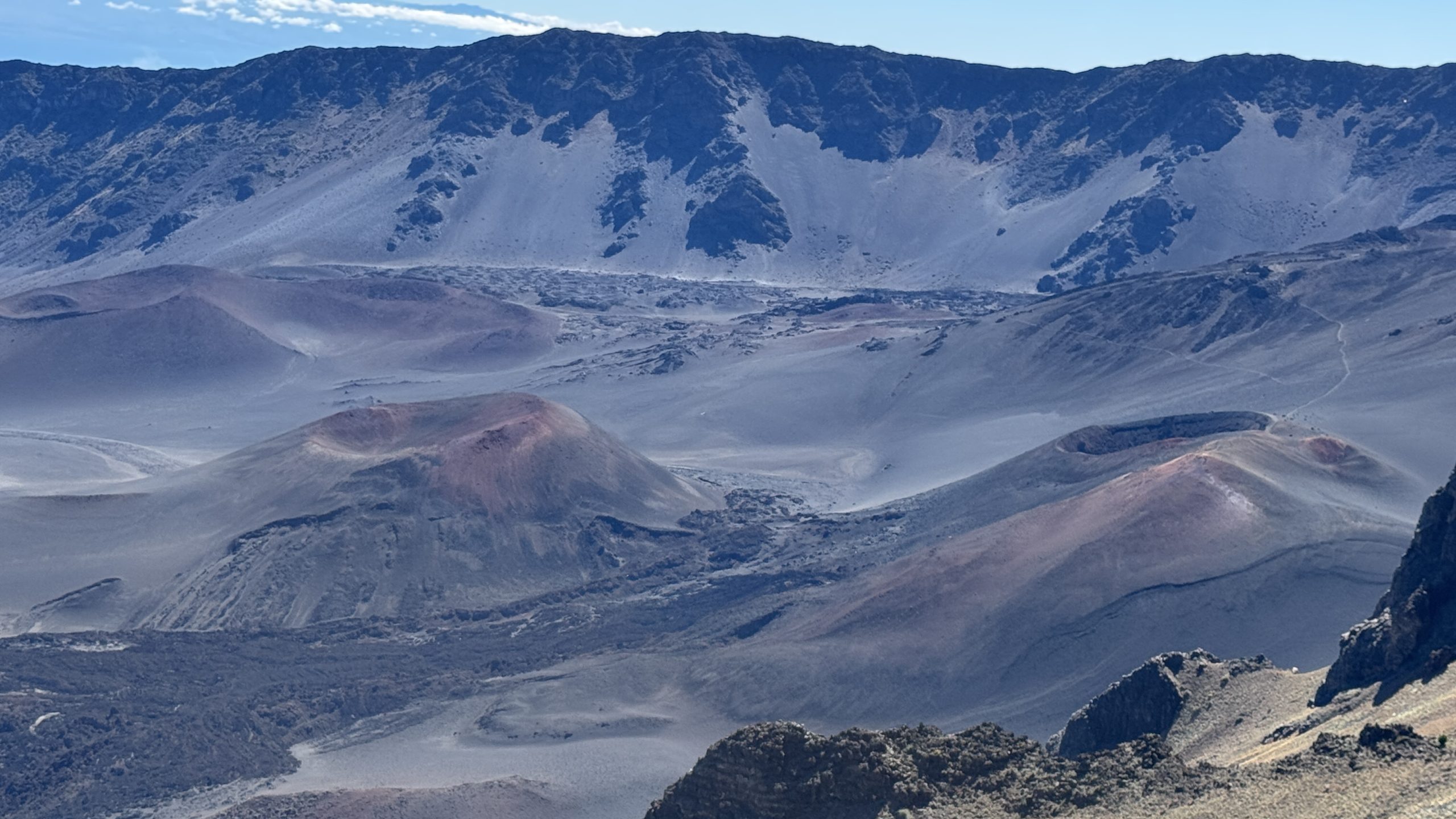 A real photograph from Leleiwi Overlook showing the Haleakalā crater ridges and cinder cones in early morning light, with clouds lingering below the rim