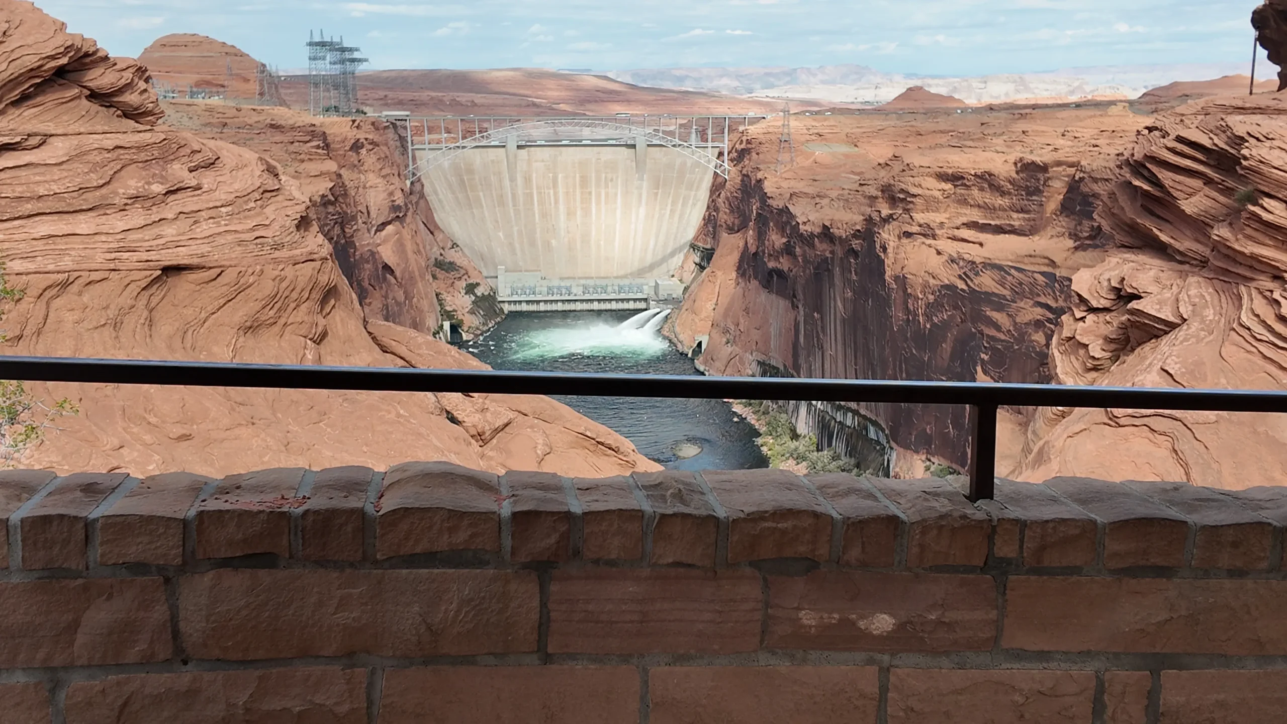 A real photograph from an overlook near Glen Canyon Dam showing the massive concrete dam and the deep canyon below near Page, Arizona under clear blue sky