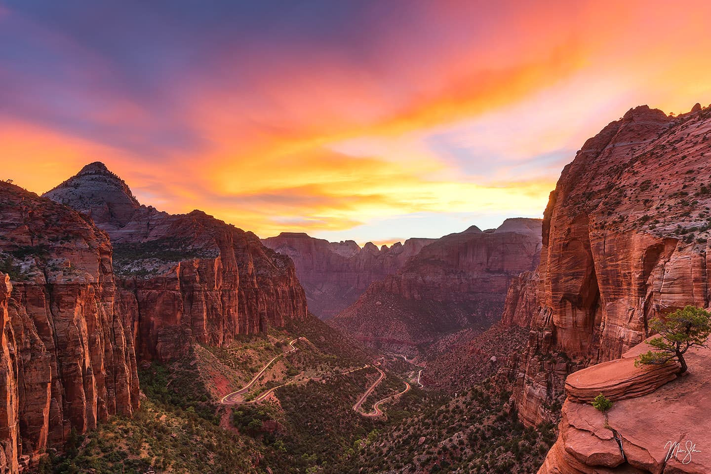 A real photograph from the Canyon Overlook viewpoint near the Zion-Mount Carmel Tunnel, with warm sunset light on layered sandstone cliffs and a few hikers standing back from the rim
