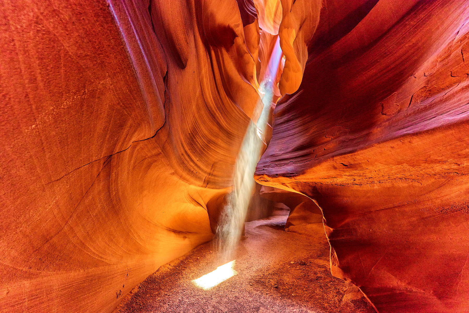 A real photograph inside Upper Antelope Canyon near Page, Arizona with sunbeams filtering down into the narrow sandstone slot and visitors following a guide