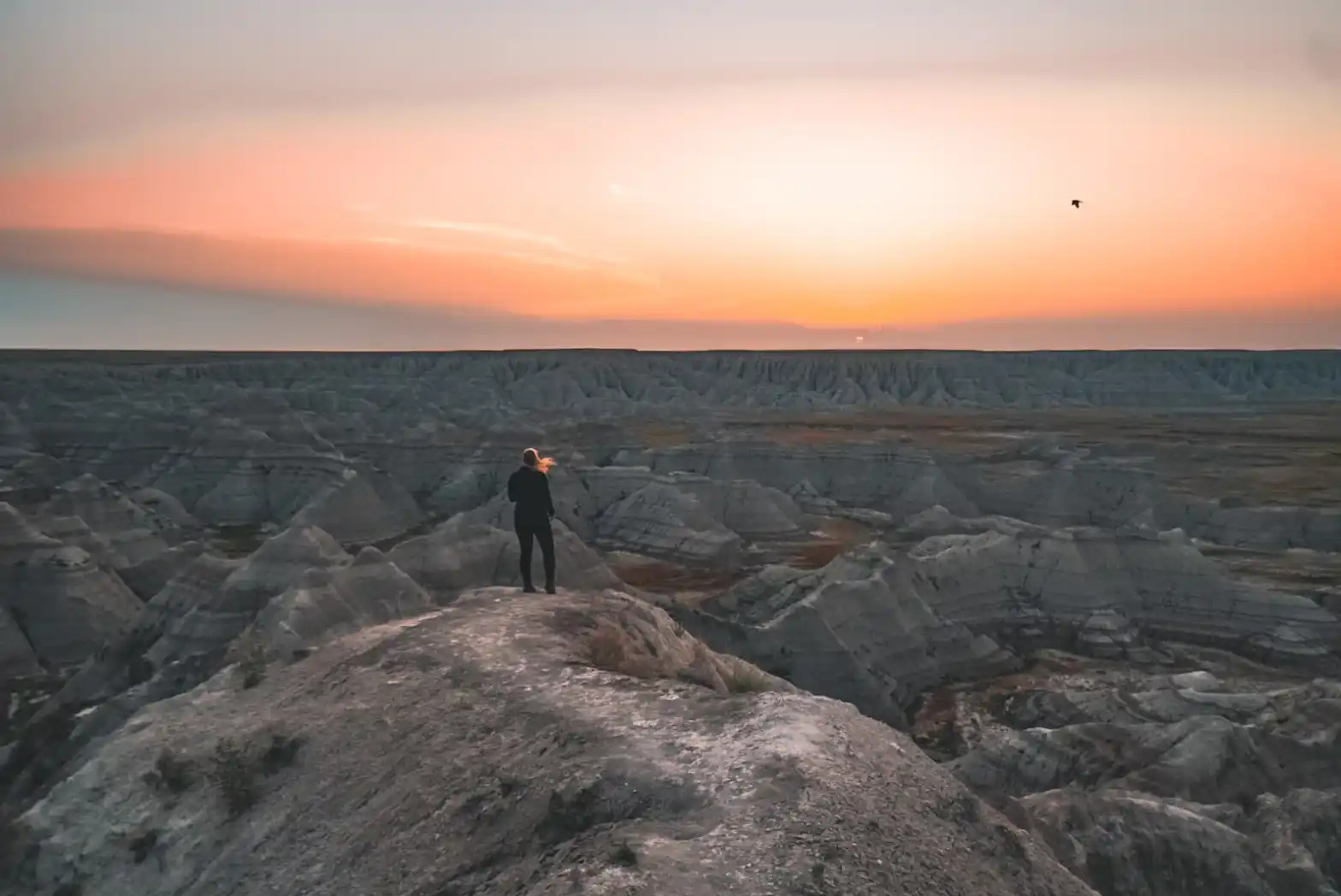 A real photograph of Big Badlands Overlook at sunrise, with pink and orange light illuminating jagged ridges and deep shadows in the valleys