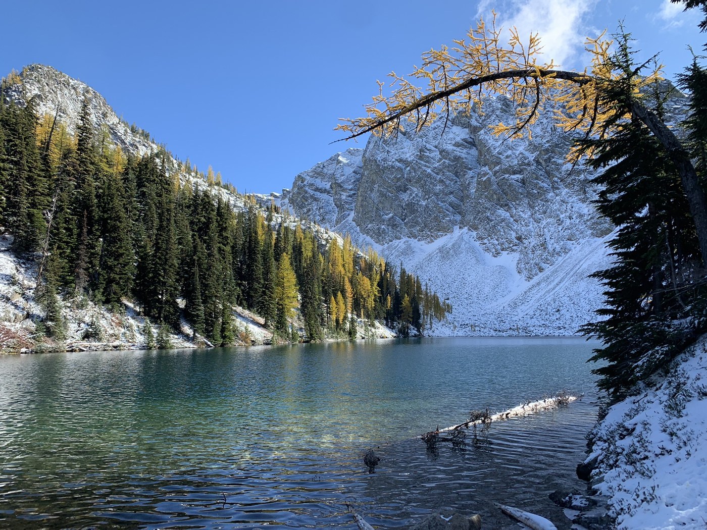 A real photograph of Blue Lake with clear blue water, a rocky shoreline, and steep gray cliffs rising behind it under bright daylight