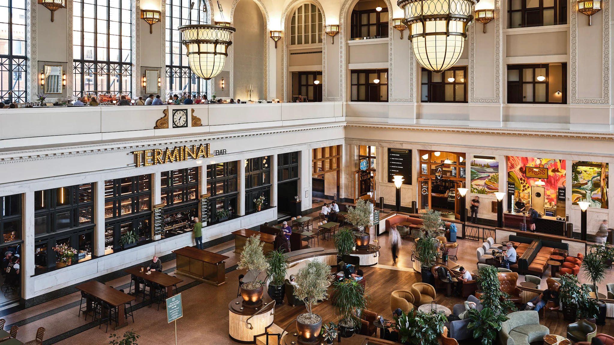 A real photograph of Denver Union Station interior with high arched windows, warm lighting, and travelers sitting in the central hall