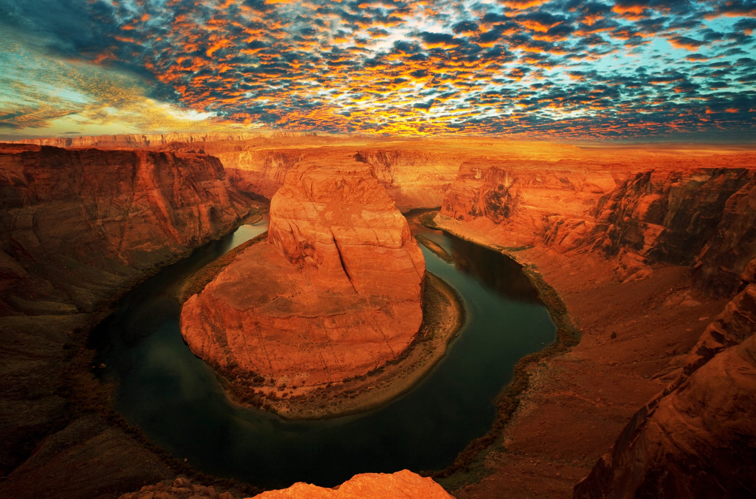 A real photograph of Horseshoe Bend near Page, Arizona at sunset, with the Colorado River curving around the sandstone cliff and visitors standing along the fenced overlook