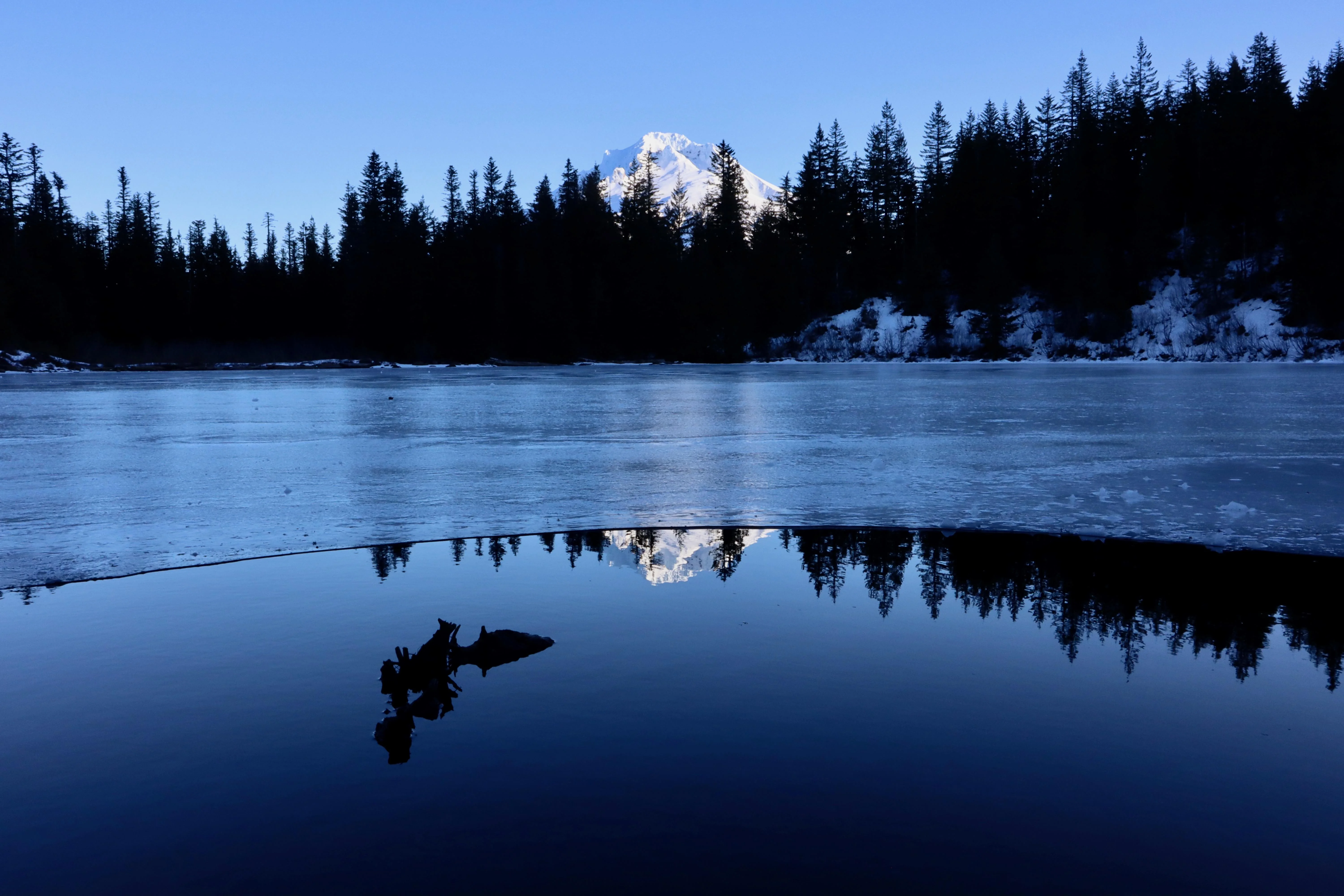 A real photograph of Mount Hood reflected in the still water of Mirror Lake at sunrise with trees framing the shoreline