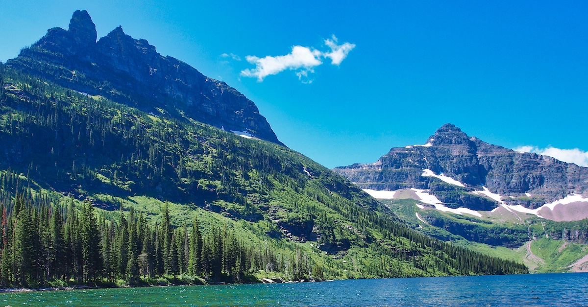 A real photograph of Two Medicine Lake in Glacier National Park in September, with calm water reflecting surrounding peaks and a thin line of autumn color along the shoreline