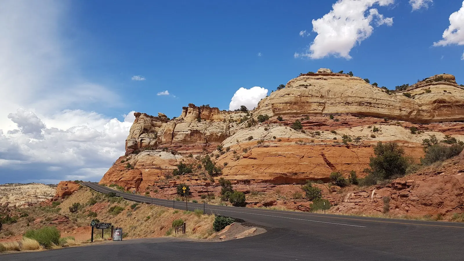 A real photograph of Utah Highway 12 near Calf Creek, with red rock cliffs and a roadside pullout under a clear blue sky, midday travel photography