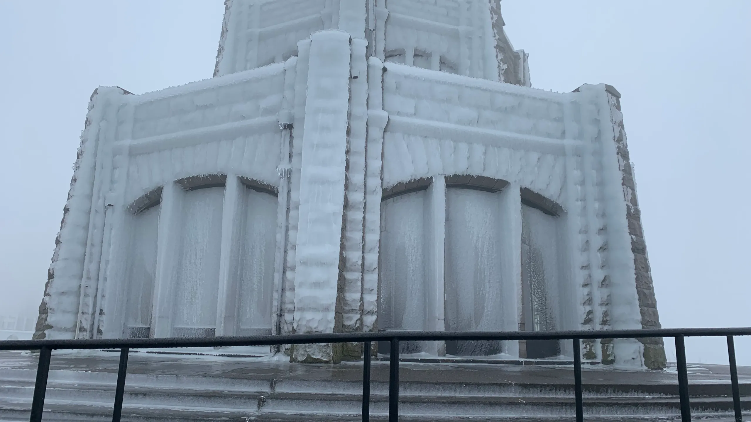 A real photograph of Vista House at Crown Point on a cold, windy day with dramatic clouds over the Columbia River and visitors bundled in jackets on the stone overlook