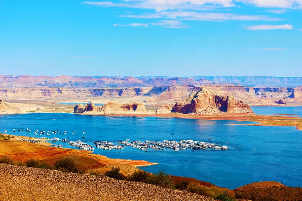 A real photograph of a Lake Powell overlook near Wahweap in Page, Arizona with blue water winding between tan sandstone cliffs under a clear sky