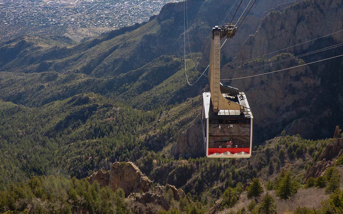 A real photograph of a Sandia Peak Tramway cabin suspended over the rugged Sandia Mountains with Albuquerque visible in the distance