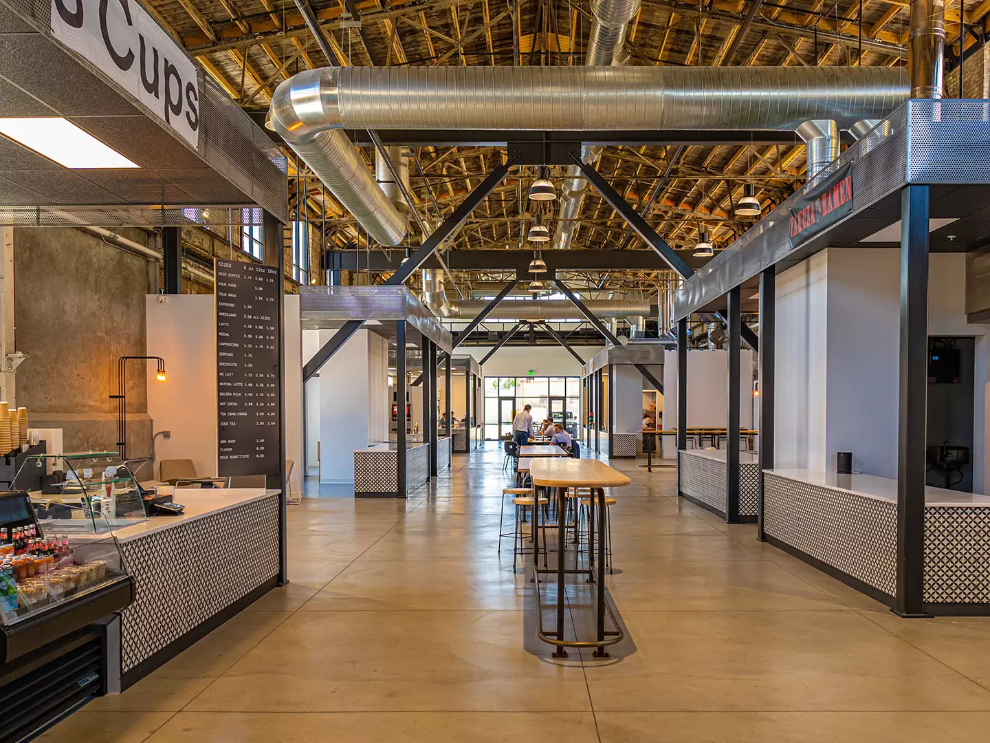 A real photograph of a busy downtown Salt Lake City food hall interior with shared tables, warm lighting, and multiple vendor counters in the background